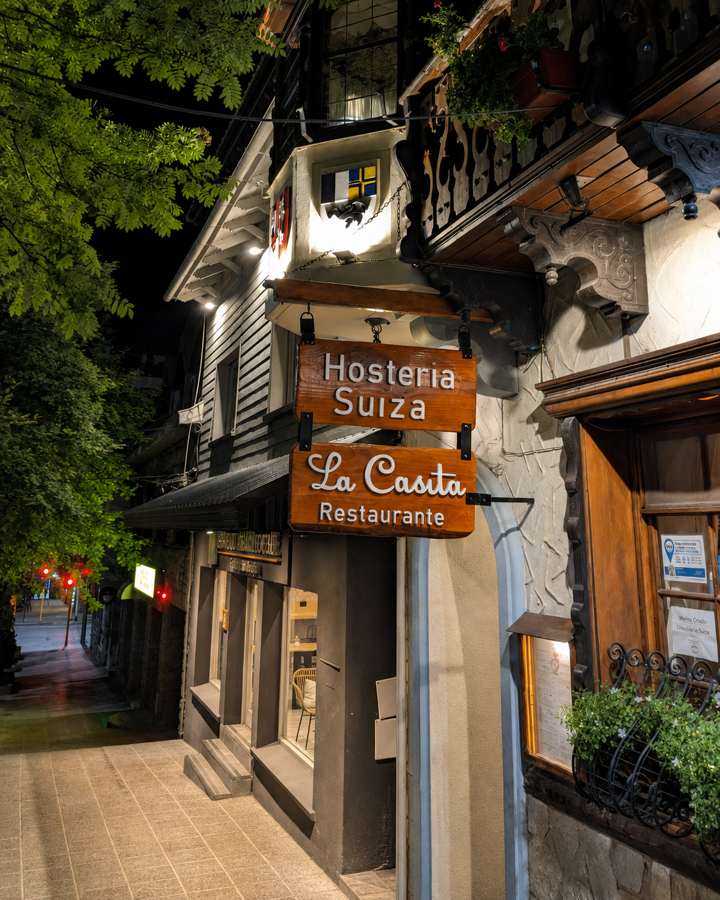 Cartel colgante de madera de Hostería Suiza y La Casita Restaurante de noche