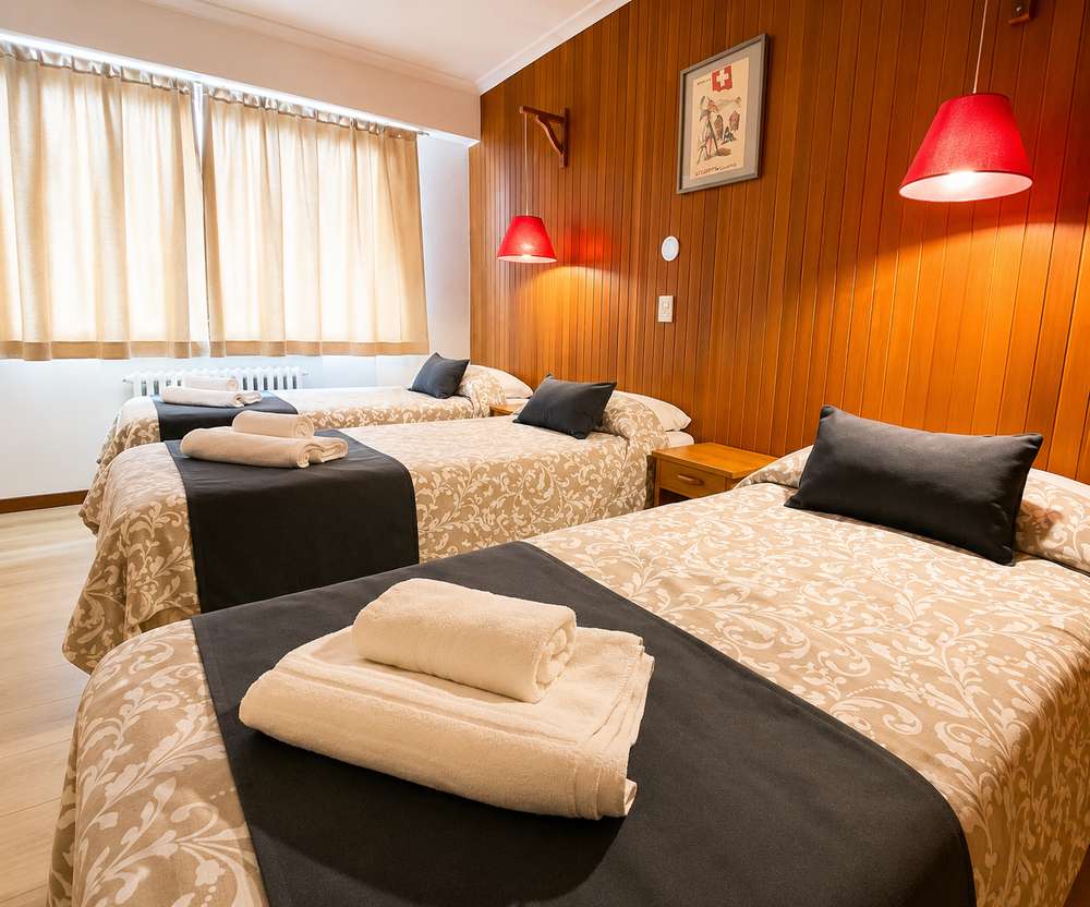 Habitación triple con tres camas individuales, pared revestida en madera y lámparas cálidas